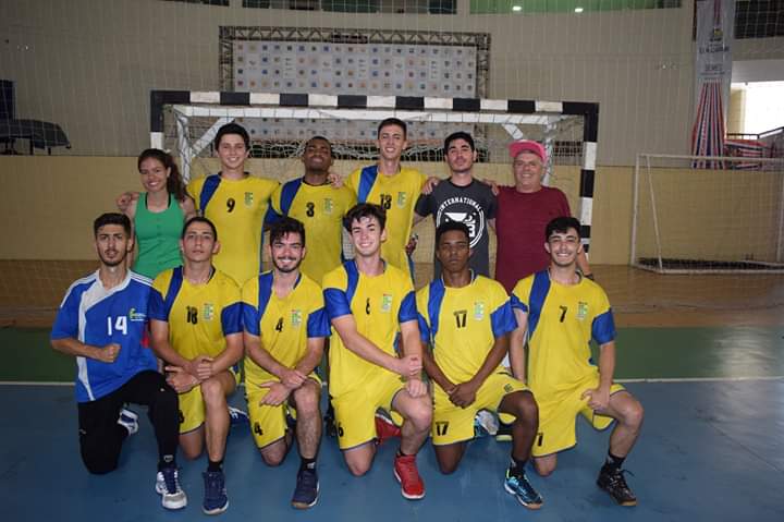 Na quadra jogadores e equipe técnica do time de handball do IFSULDEMINAS posam em frente ao gol